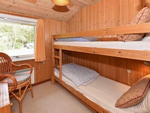 Une chambre avec un lit superposé, une fenêtre, une chaise et un coussin à motifs.
