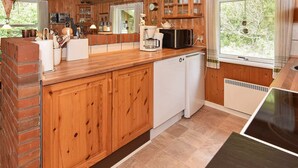 A wooden cabin kitchen with a brick wall, wooden cabinets, a white dishwasher, and a window with curtains.