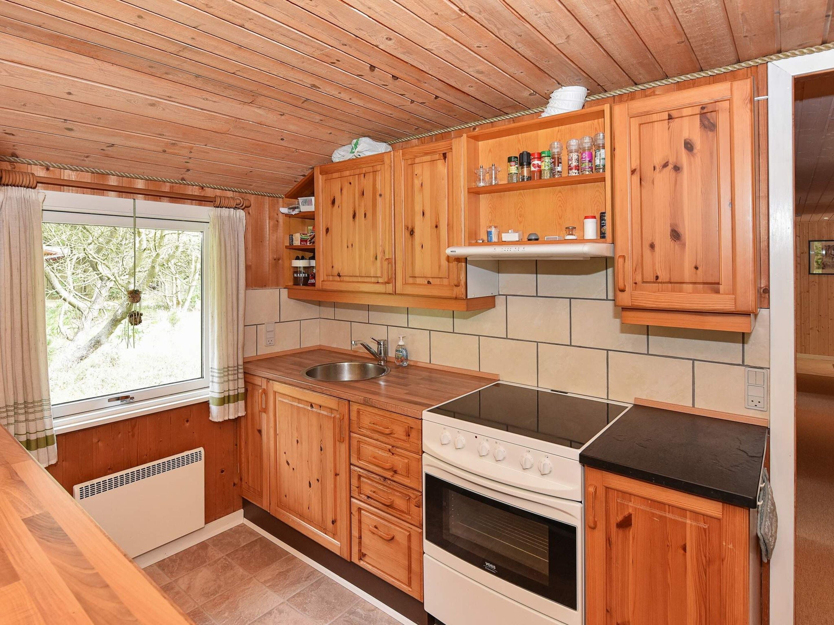 Une cuisine compacte avec des meubles en bois, un four encastré et une fenêtre avec un rideau.