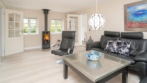 A living room with a glass coffee table, a black leather sofa, a black leather chair, a white door with glass panels, a white ceiling, a fireplace, and a painting on the wall. - 5 Person Holiday Home in Vig (Vig)