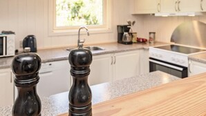 A kitchen with wooden cabinets, a window, a sink, a stove, and two black pepper mills on the counter. - 8 Person Holiday Home in Blavand (Blavand)