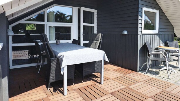 A covered patio with a table and chairs, large windows, and a view of the outdoors. - 8 Person Holiday Home in Blavand (Blavand)