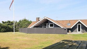 A house with a sloped roof, a fenced yard, and a flagpole. - 8 Person Holiday Home in Blavand (Blavand)