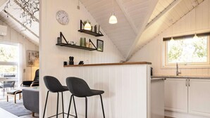 A modern kitchen with white cabinetry, a wooden countertop, and two bar stools. There is a clock on the wall and a window providing natural light. - 8 Person Holiday Home in Blavand (Blavand)