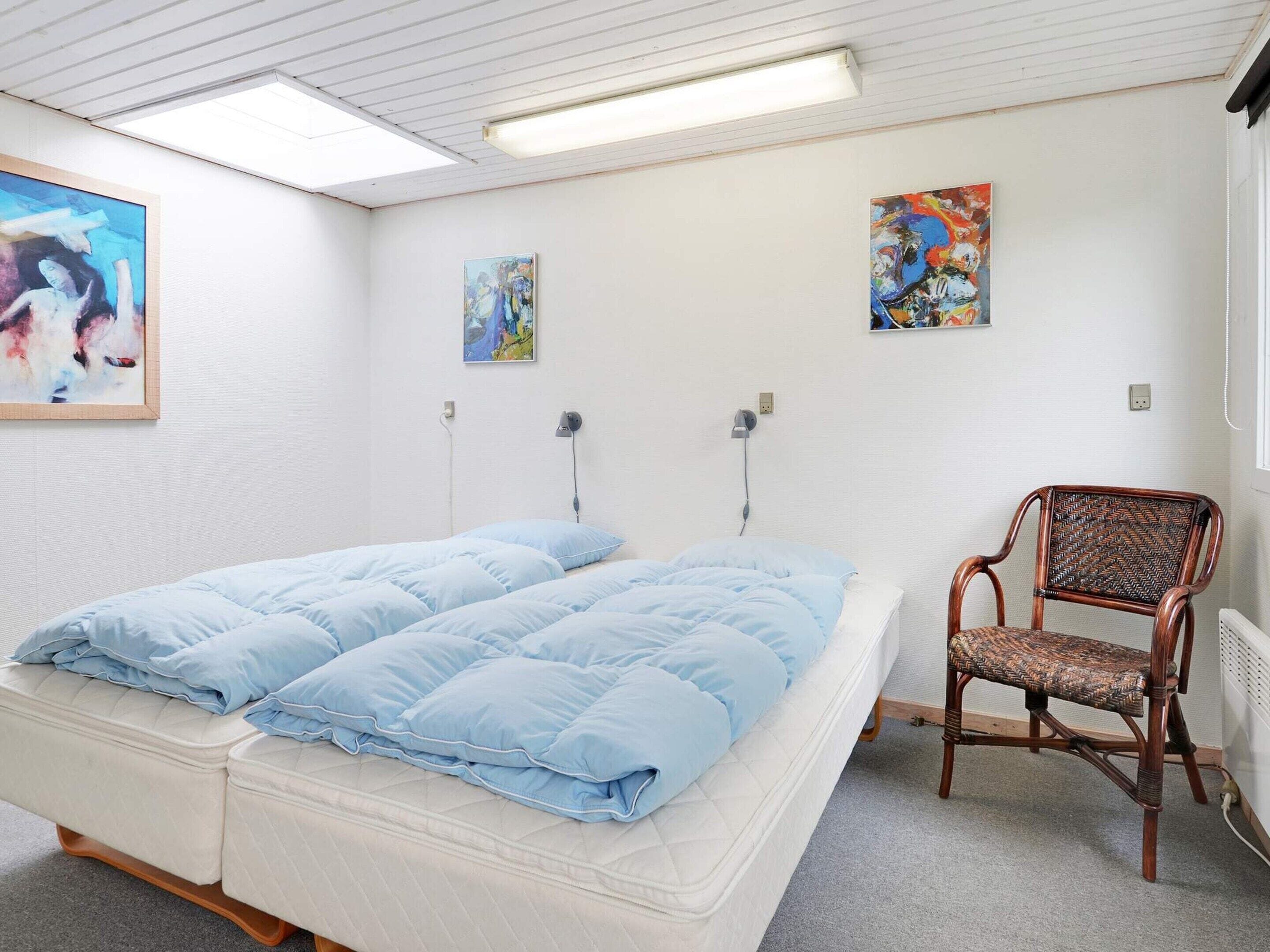 Een kamer met een bed, een stoel en twee schilderijen aan de muur.