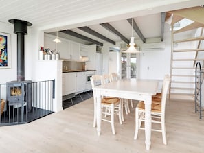 A modern kitchen with white cabinetry, a black stove, and a dining area with white chairs.