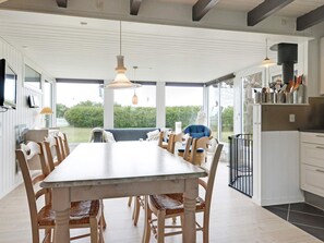 A modern kitchen with a dining area, large windows, and a view of the outdoors.