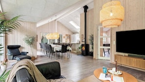 A modern living room with a fireplace, a dining area, and a TV. - 5 Star Holiday Home in Henne (Henne)