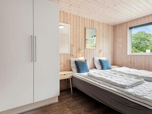 A bedroom with a wooden ceiling, a bed with white bedding, a nightstand, a desk, and a window with a view of trees. - 5 Star Holiday Home in Henne (Henne)
