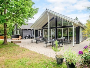 A modern outdoor patio area with multiple tables and benches, surrounded by a wooden deck and potted plants. - 5 Star Holiday Home in Henne (Henne)