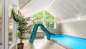 An indoor swimming pool with a blue slide, large windows, and a potted plant. - 5 Star Holiday Home in Henne (Henne)