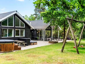 A black building with large windows, a covered outdoor seating area, and a swing set. - 5 Star Holiday Home in Henne (Henne)