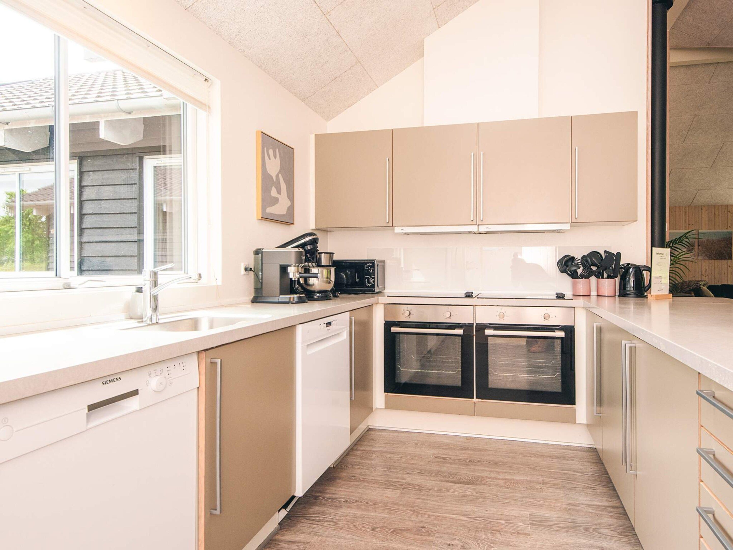 A modern kitchen with white cabinets, a dishwasher, a coffee machine, and two ovens.