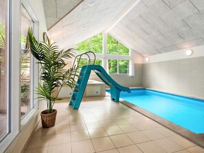 An indoor swimming pool with a blue slide, large windows, and a potted plant. - 5 Star Holiday Home in Henne (Henne)