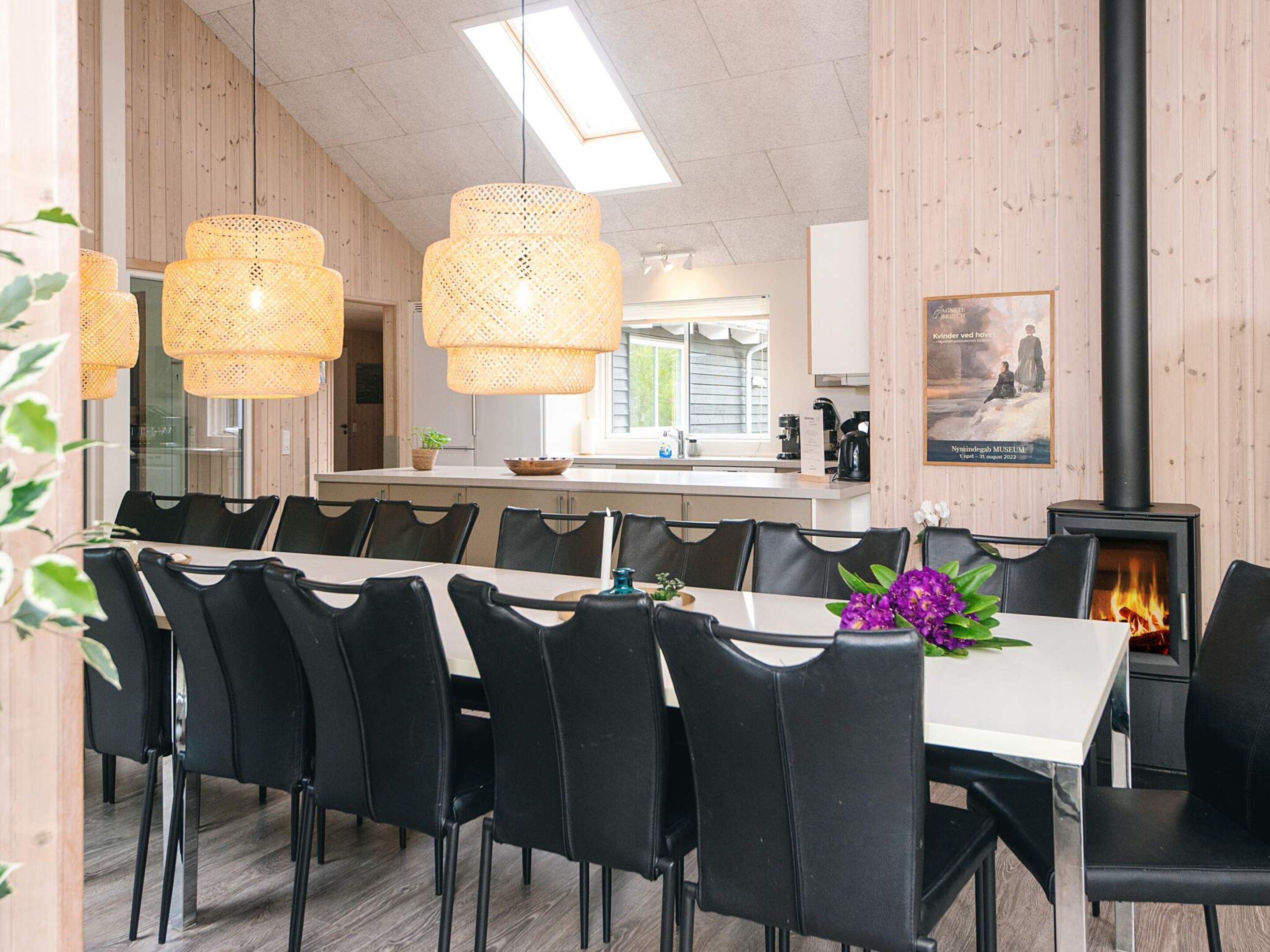 A dining area with a long table, black chairs, woven pendant lights, and a wood-burning stove.