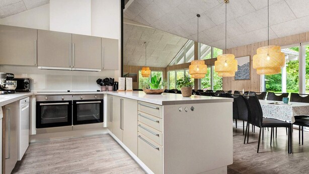 A modern kitchen with built-in appliances, a dining area with a table and chairs, and large windows allowing natural light. - 5 Star Holiday Home in Henne (Henne)
