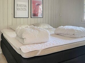A bed with white bedding and pillows, a framed picture with text, and a lamp on the wall.