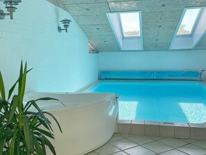 A swimming pool with a white tub, skylights, and a potted plant.