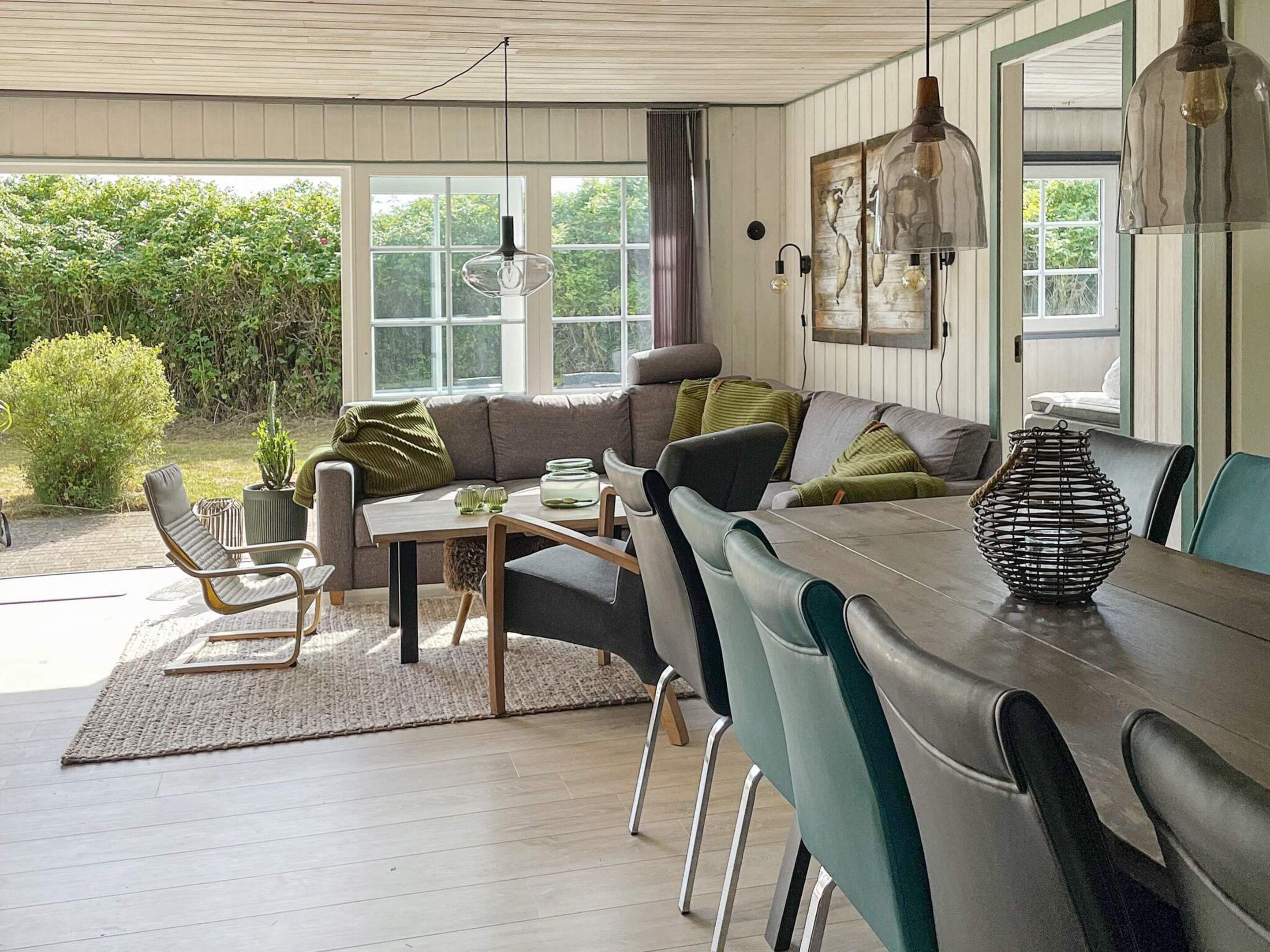 A cozy living room with a sofa, chairs, a dining table, and a view of greenery outside.