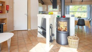 A modern kitchen with a wood-burning stove, a dining area with a table and chairs, and a view of the outdoors through large windows.