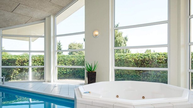 A modern indoor swimming pool with a large jacuzzi, large windows, and a potted plant.