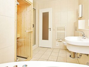 A modern bathroom with a wooden sauna door, a white sink, and a glass shower enclosure. - Holiday Home in Grossenbrode (Grossenbrode)