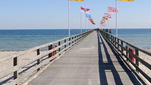 A wooden pier extending into the sea with multiple flags on poles. - Holiday Home in Grossenbrode (Grossenbrode)
