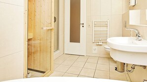 A bathroom with a wooden sauna door, a white sink, and a mirror. - Holiday Home in Grossenbrode (Grossenbrode)