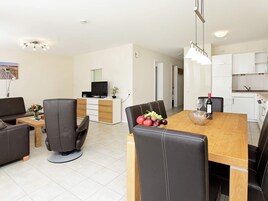 Una sala de estar moderna con un sofá, una mesa de comedor con sillas, un televisor y una cocina con armarios y una encimera.