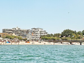Un hôtel situé en bord de mer, avec plusieurs étages, une plage de sable et un pont.