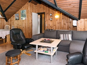 A cozy room with a wooden ceiling, a black leather chair, a grey sofa, a small wooden stool, and a table with magazines.