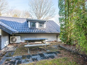 A house with a blue tiled roof, a window, a patio with a bench, and a tree.