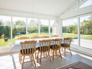 A conservatory with a table and chairs, large windows, and a view of a garden.