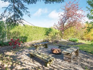 A picnic area with benches and a fire pit surrounded by gravel, with trees and a mountain in the background.