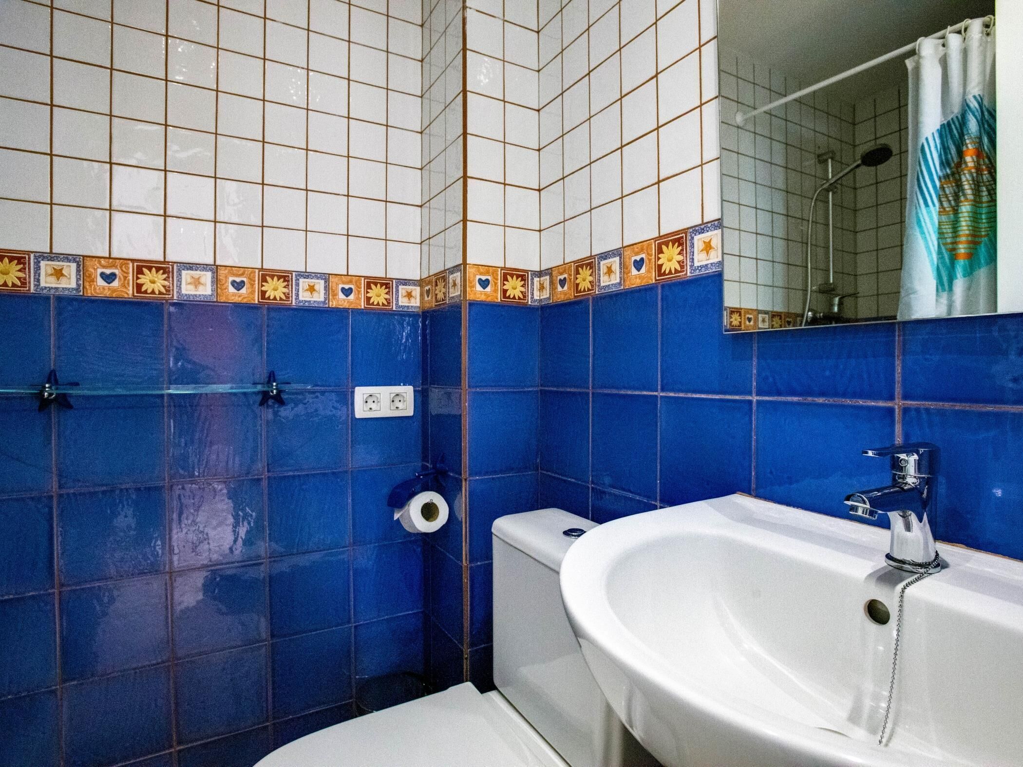 Casa de banho com paredes revestidas de azulejos azuis, uma pia branca e uma sanita.