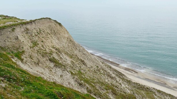 A coastal landscape with a steep cliff, a sandy beach, and calm sea.