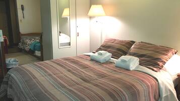 A hotel room with a bed, two bedside lamps, a mirror, and a telephone on the wall.