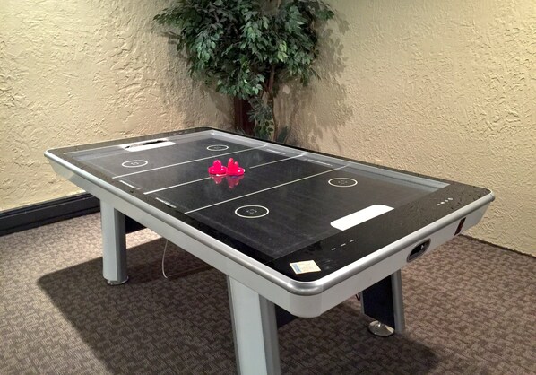 Une table de ping-pong avec un filet au centre, un petit objet rouge posé sur la table et une plante en pot à l’arrière-plan.