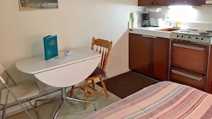 A compact kitchen with a dining table, a chair, and a bed with a striped blanket. - #09 - Snowline Lodge (Deming)