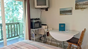 A bedroom with a bed, a desk, a chair, a television, and a window with a view of trees. - #09 - Snowline Lodge (Deming)