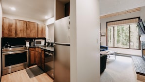 A modern kitchen with stainless steel appliances, wooden cabinets, and a dining area with a view of trees through large windows. - Condo - Pets OK - Fireplace, Sleeps 4! (Deming)