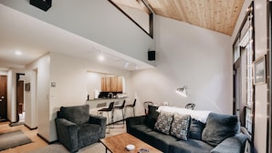 A modern living room with a sofa, armchairs, a wooden coffee table, and a dining area with chairs and a kitchen in the background. - Condo - Pets OK - Fireplace, Sleeps 4! (Deming)