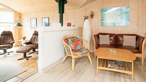 Ett mysigt rum med träväggar och träpanel i taket, en soffa, två fåtöljer, ett litet bord och en öppen spis.