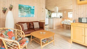 En mysig trästuga med en soffa, flätade stolar, ett träbord, en köksdel och ett matbord.