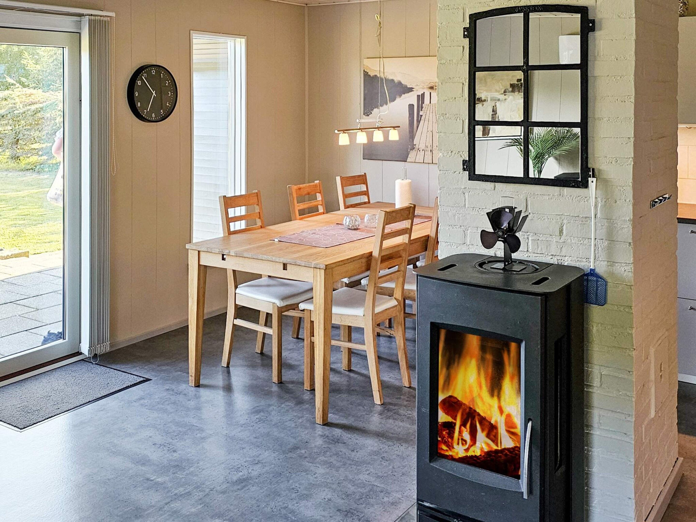 Un comedor con una mesa y sillas, una estufa de leña, un reloj y una ventana con persianas.