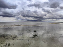 Un paisaje costero con una extensa masa de agua, una playa arenosa y cielos nublados.