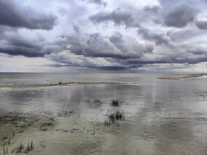 A coastal landscape with a wide expanse of water, a sandy beach, and overcast skies.