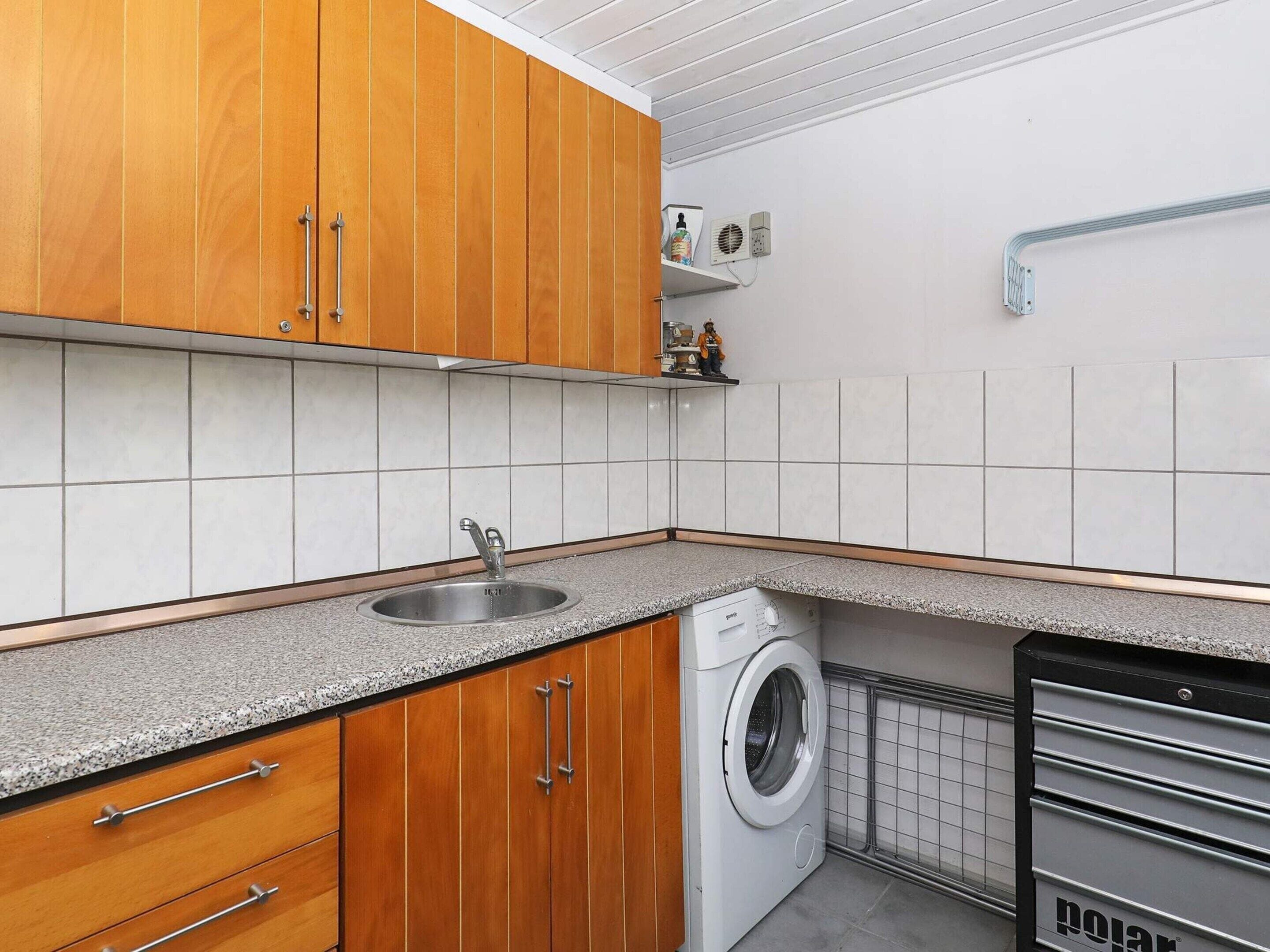 Une cuisine compacte avec des meubles en bois, un évier en acier inoxydable, un lave-linge et une petite étagère contenant des articles de toilette.