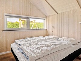 Un dormitorio con cama, paredes de madera, ventana con vista a un jardín y techo con vigas a la vista.