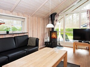 A cozy living room with a black leather sofa, a wooden coffee table, a television, and a wood-burning stove. - 5 Star Holiday Home in Juelsminde (Horsens)